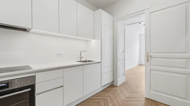 Moderne weiße Küche mit integrierten Geräten und Fischgrätparkett, offen zu einem weiteren Raum.
