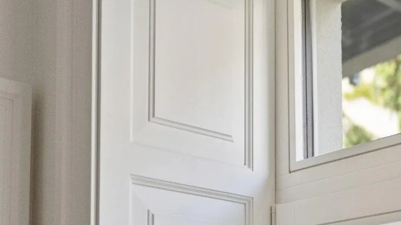 Detailansicht eines weißen Fensters mit dekorativen Paneelen und einem Blick ins Grüne.