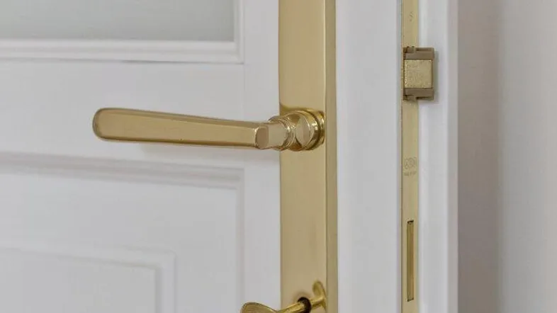 Detailaufnahme einer weißen Tür mit elegantem goldenem Türgriff und Schlüssel im Schloss.