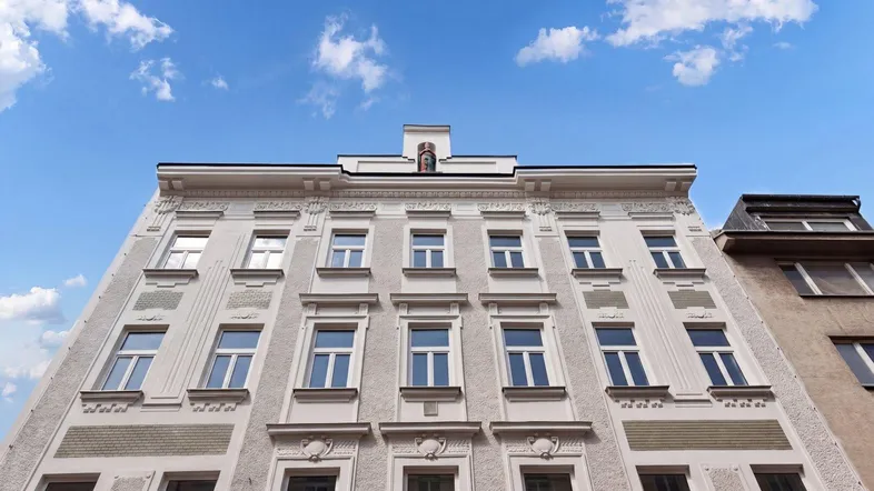 Historische Fassade eines gepflegten Gebäudes mit vielen Fenstern und dekorativen Elementen unter blauem Himmel.