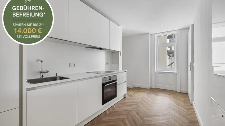 Moderne Küche mit weißen Schränken, Fischgrätparkett und viel Tageslicht durch das große Fenster.