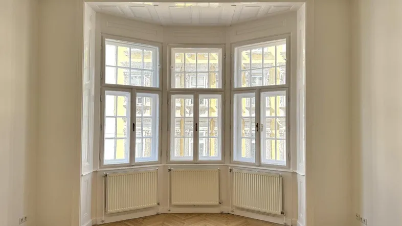 Helles Zimmer mit Erkerfenstern, Fischgrätparkett und hohen Decken, ideal als Wohn- oder Schlafzimmer.