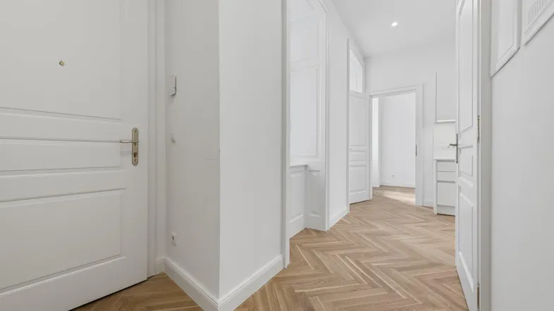 Heller Flur mit elegantem Fischgrätparkettboden und weißen Türen, der zu weiteren Räumen führt.