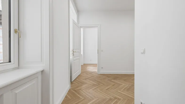 Heller Raum mit elegantem Fischgrätparkettboden, weißen Wänden und klassischer Wandvertäfelung.
