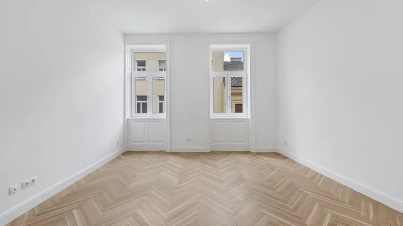 Heller, frisch renovierter Raum mit hohen Decken, Fischgrätparkett und zwei großen Fenstern mit Stadtblick.