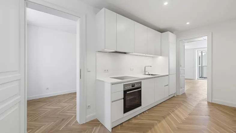 Moderne, helle Küche mit weißen Schränken, integrierten Geräten und elegantem Fischgrätparkettboden.