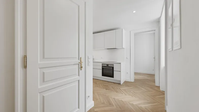 Heller Eingangsbereich mit Fischgrätparkett und Blick in eine moderne weiße Küche.