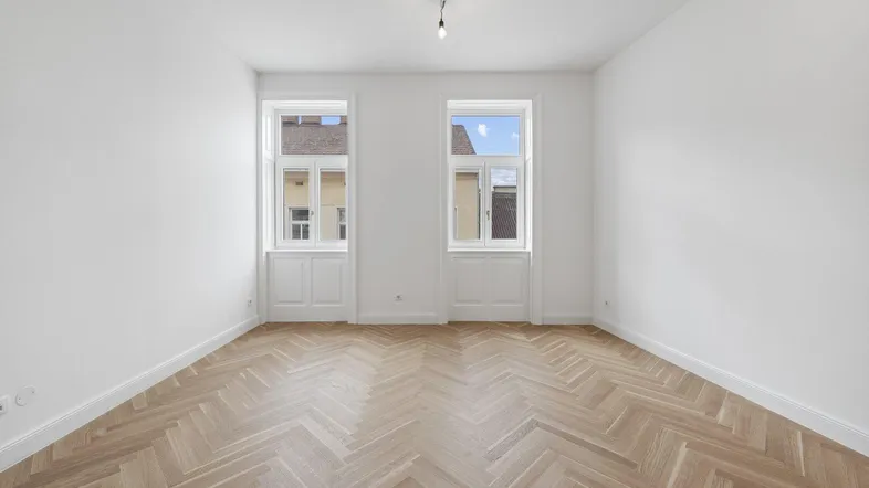 Heller, frisch renovierter Raum mit elegantem Fischgrätparkett und hohen Decken.