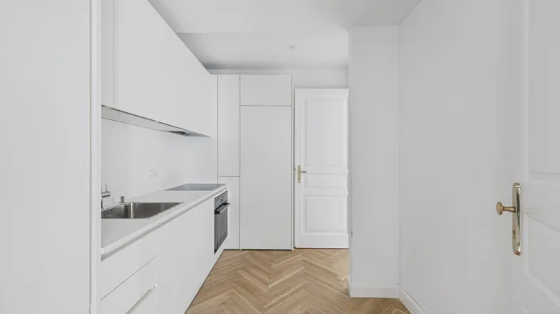 Helle, moderne Küche mit weißen Einbauschränken, integrierten Geräten und elegantem Fischgrätparkett.
