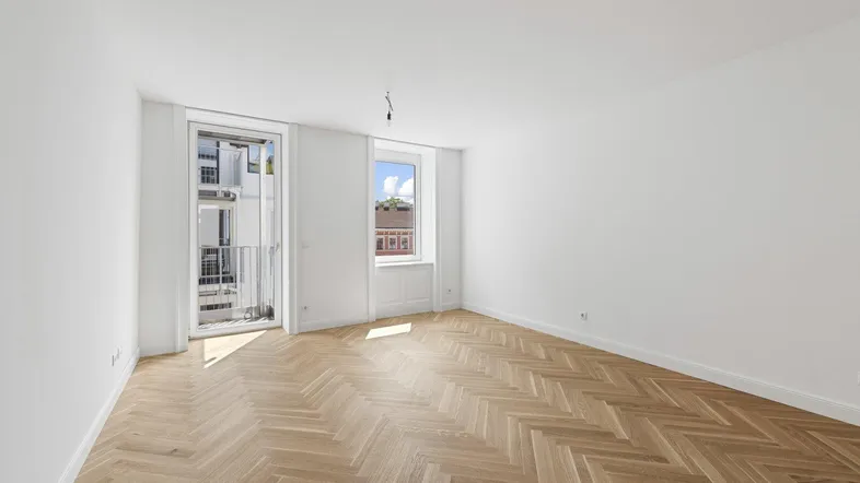 Heller Raum mit Fischgrätparkett, weißen Wänden und Zugang zu einem französischen Balkon.