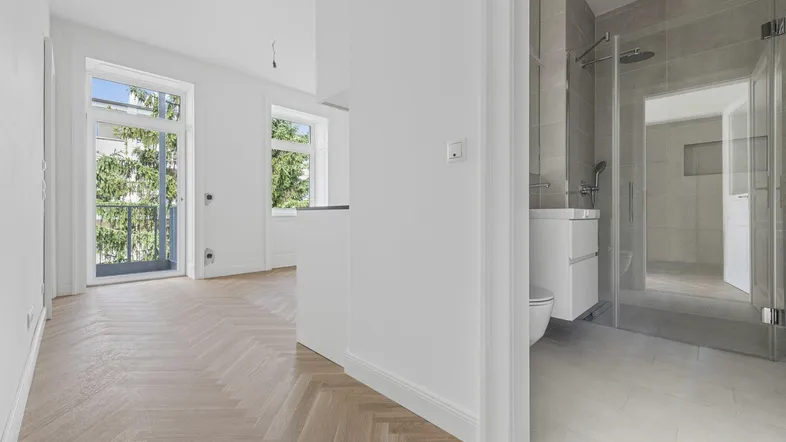 Heller Innenraum mit Fischgrätparkett, Balkonzugang und einem modernen Badezimmer mit begehbarer Dusche.
