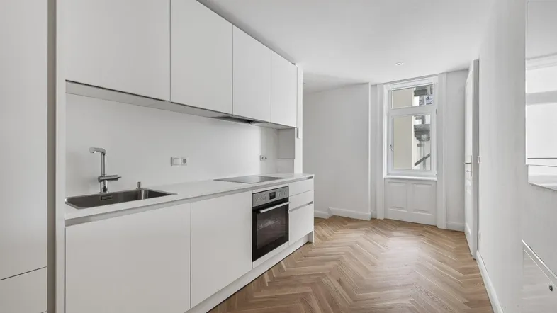 Helle, moderne Küche mit weißen Schränken, integrierten Geräten und elegantem Fischgrätparkett.