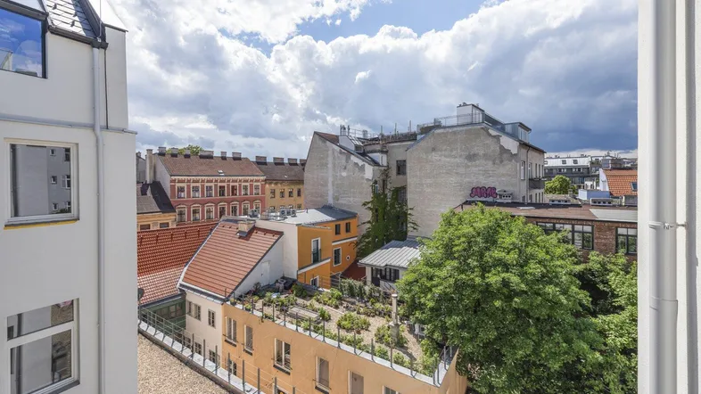 Blick von einem oberen Stockwerk über die Dächer der Stadt mit verschiedenen Gebäuden und begrünten Flächen unter bewölktem Himmel.