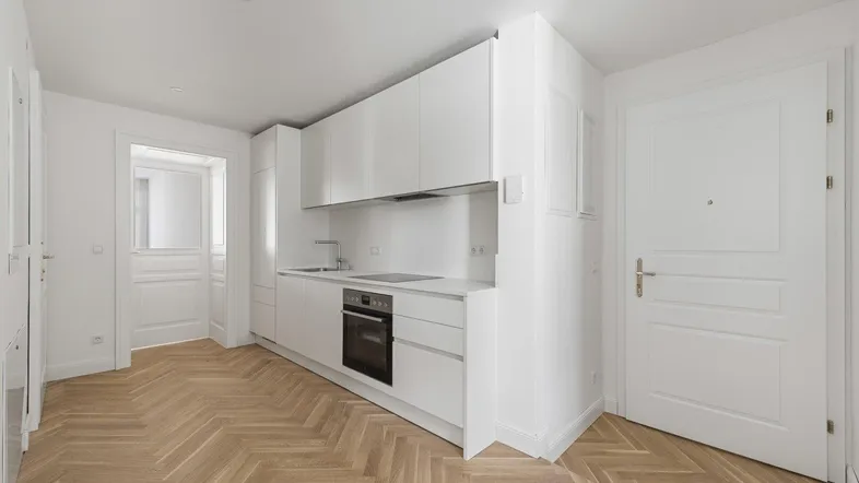 Moderne Küche mit weißen Schränken und integrierten Geräten. Der Raum verfügt über helles Fischgrätparkett und ist lichtdurchflutet.