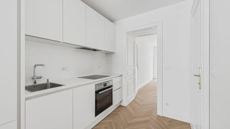 Moderne weiße Küche mit Einbaugeräten, Fischgrätparkett und Zugang zu einem Flur.