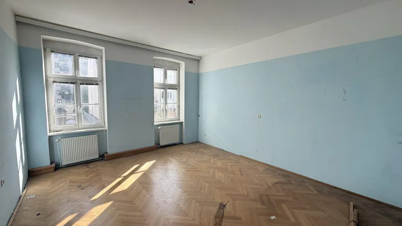 Geräumiges Zimmer mit Fischgrätparkett und blauen Wänden, bereit für Renovierung.