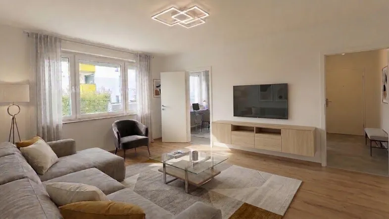 Helles Wohnzimmer mit Parkettboden, bequemer Couch und Blick ins Grüne durch große Fenster.