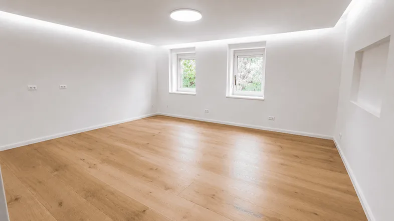 Heller, unmöblierter Raum mit Holzboden und modernen Deckenleuchten, bereit zur individuellen Gestaltung.