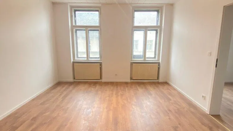 Leerer Raum mit Laminatboden, zwei Fenstern und Deckenbeleuchtung, bereit zur individuellen Gestaltung.