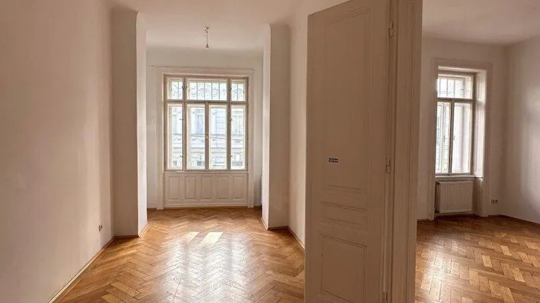 Helles Zimmer mit Fischgrätparkett und hohen Fenstern, das viel Tageslicht hereinlässt.