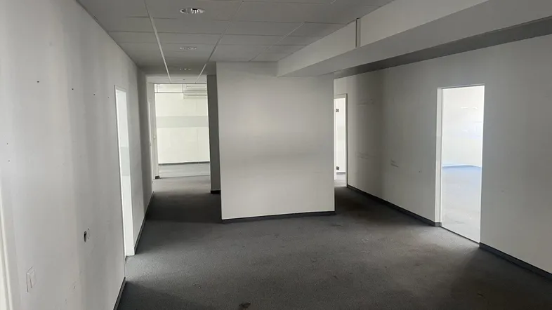 Geräumiger Büroraum mit grauem Teppichboden, weißen Wänden und abgehängter Decke, bereit zur individuellen Gestaltung.