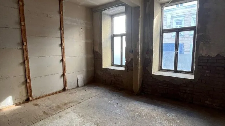 Unfertiger Innenraum mit Betonboden und zwei Fenstern, bereit für die Renovierung in einem Altbau.