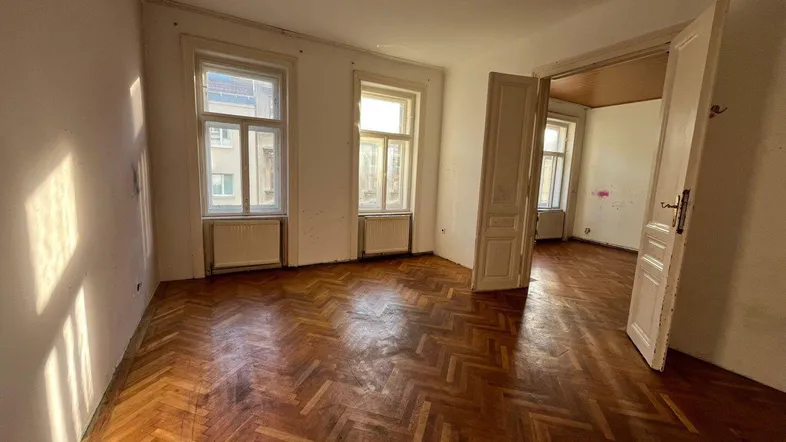 Helles Zimmer mit Fischgrätparkettboden und zwei Fenstern, bereit zur Renovierung.