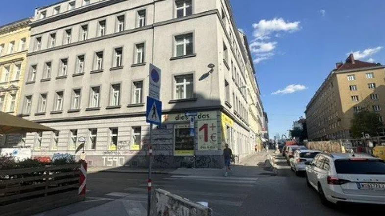 Gebäudeansicht von der Straßenecke mit geparkten Autos und blauem Himmel.