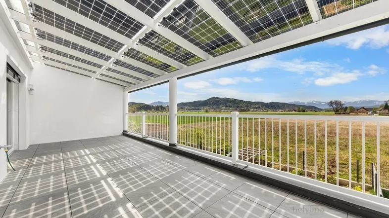 Große überdachte Terrasse mit Solarpaneelen auf dem Dach und weitem Blick ins Grüne.