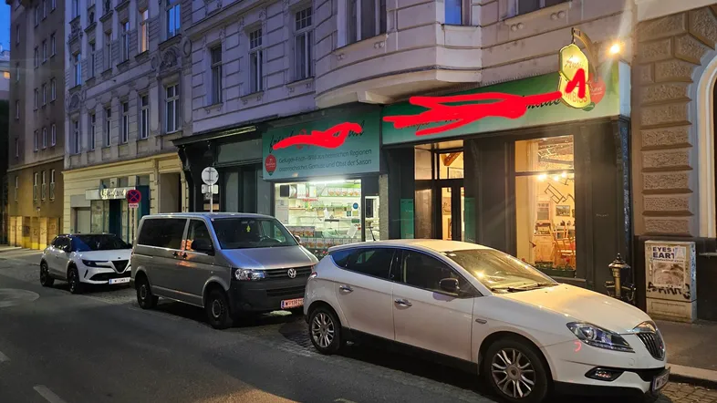Abendliche Straßenansicht mit geparkten Autos vor einem Geschäftsgebäude in der Stadt.