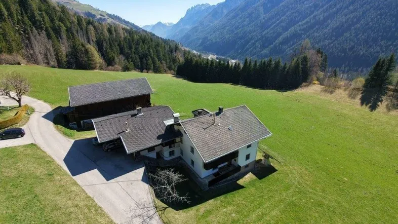 Luftaufnahme eines Anwesens mit mehreren Gebäuden in einer malerischen Berglandschaft und grünen Wiesen.