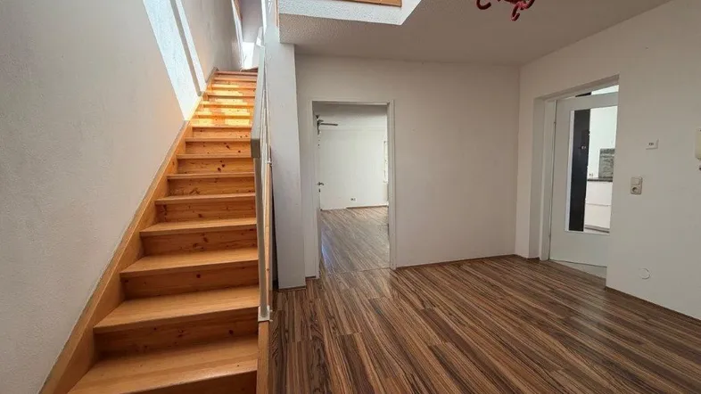 Heller Eingangsbereich mit Holztreppe und Laminatboden, der zu den oberen Etagen führt.
