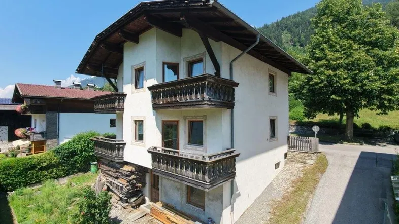 Traditionelles Haus mit Holzbalkonen und Bergblick, umgeben von grüner Landschaft.