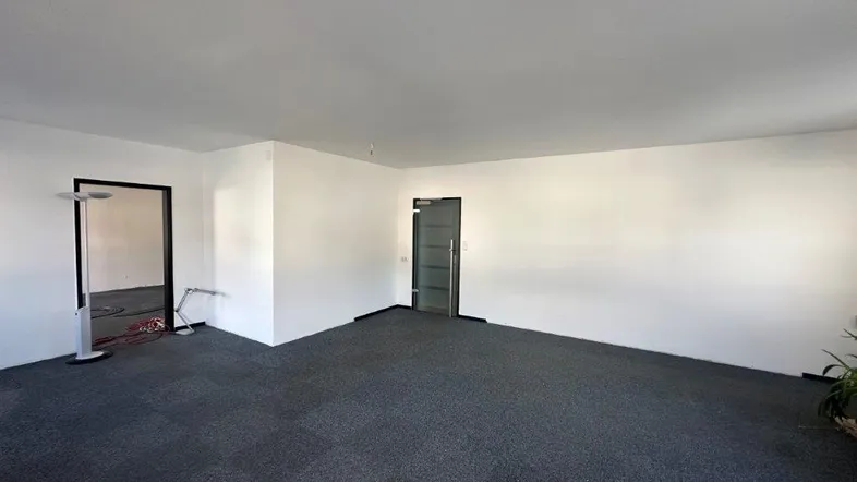 Geräumiger Büroraum mit dunklem Teppichboden und weißen Wänden, bereit für die individuelle Gestaltung.