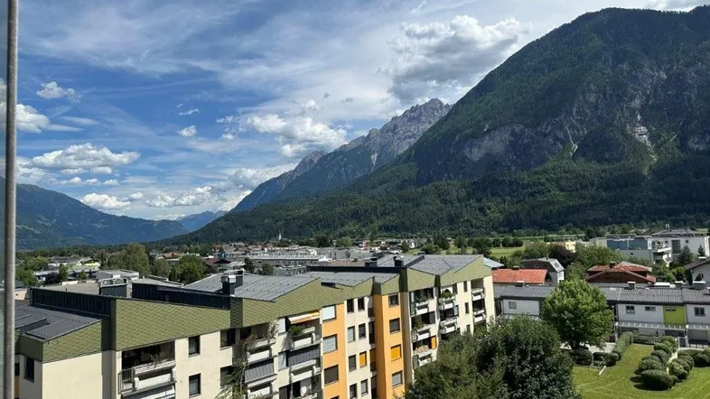 Blick auf die umliegende Berglandschaft und Wohngebäude unter blauem Himmel.