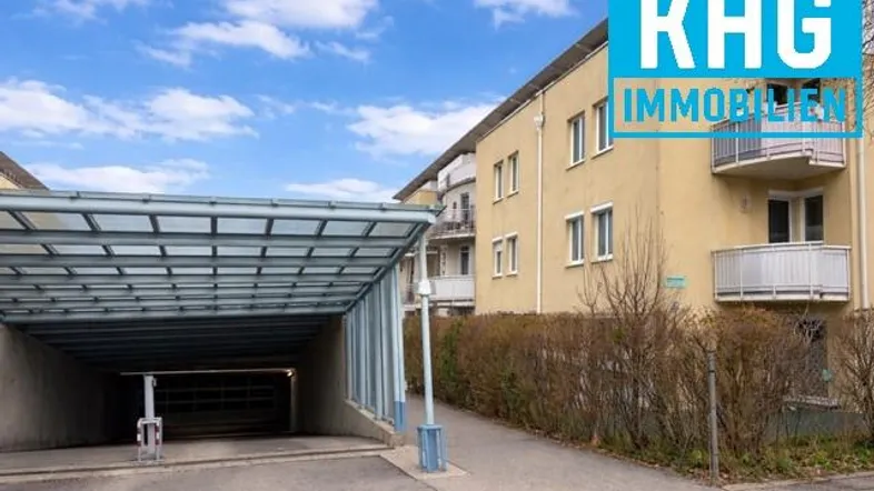 Gebäudeansicht mit gelber Fassade, Balkonen und Zufahrt zur Tiefgarage unter blauem Himmel.