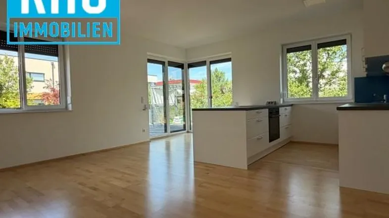 Offener Wohnbereich mit Holzboden und Zugang zu einem Außenbereich, inklusive Kücheninsel.