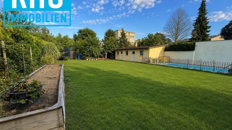 Großer grüner Garten mit Rasenfläche, Hochbeet und einem Swimmingpool im Hintergrund.