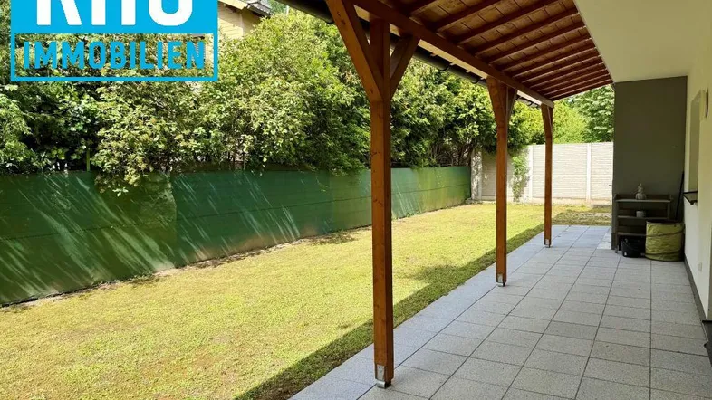 Überdachte Terrasse mit Holzbalken und Blick auf den gepflegten Rasenbereich.