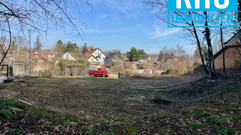 Großes, unbebautes Grundstück mit Blick auf eine Wohnsiedlung und umliegende Bäume.
