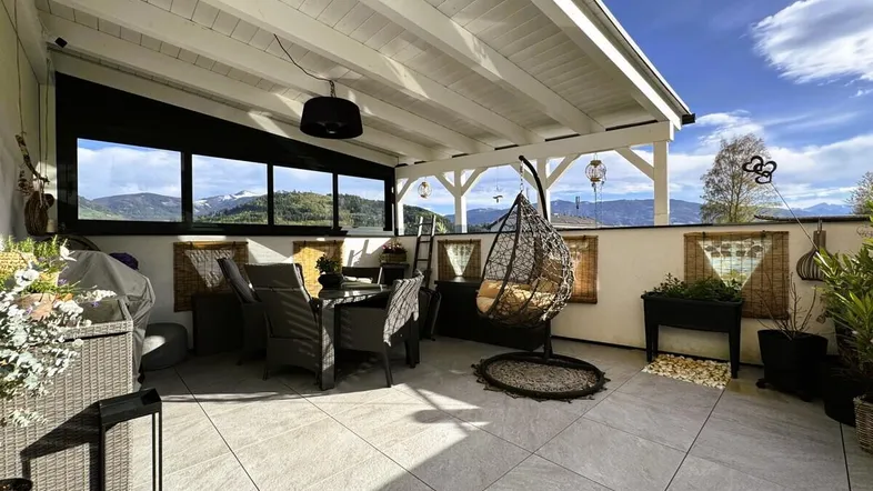Überdachte Terrasse mit Essbereich, Hängesessel und weitem Blick auf die Berge.