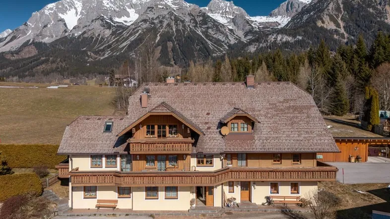 Frontansicht eines traditionellen Gebäudes mit Holzbalkonen vor einer beeindruckenden Bergkulisse.