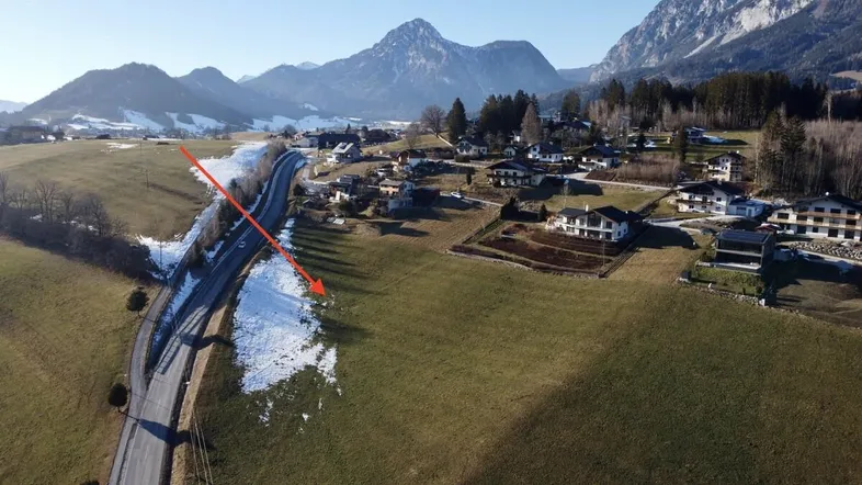 Luftaufnahme einer ländlichen Gegend mit Häusern, Feldern und schneebedeckten Bergen im Hintergrund.