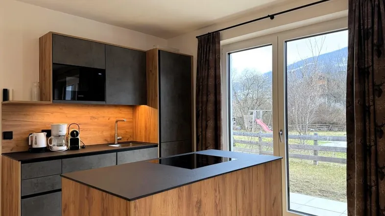 Moderne Küche mit Kochinsel, integrierten Geräten und Blick auf die verschneite Landschaft und einen Spielplatz.