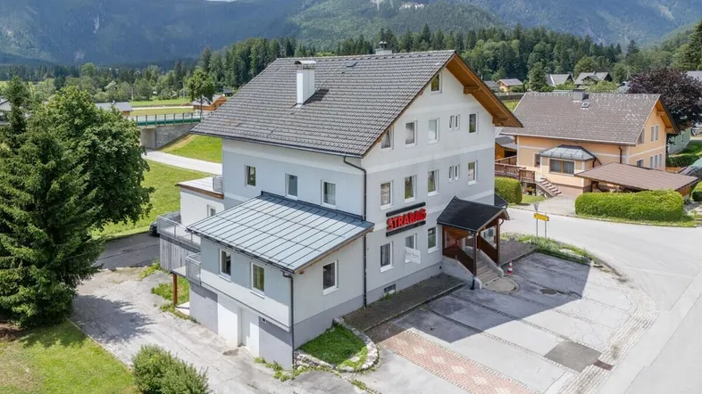 Luftaufnahme eines Mehrfamilienhauses mit Satteldach und umliegender grüner Landschaft.