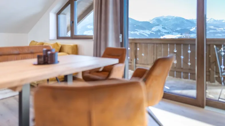Heller Essbereich mit Holztisch und bequemen Stühlen, mit direktem Zugang zum Balkon und Bergblick.