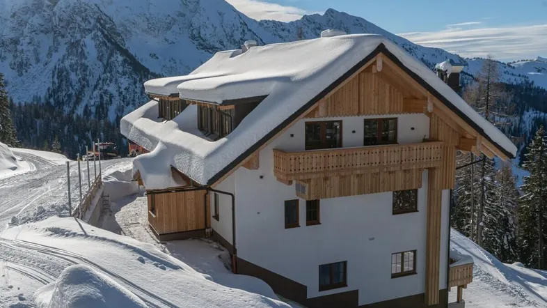 Traditionelles Chalet im alpinen Stil mit verschneitem Dach und Bergblick.