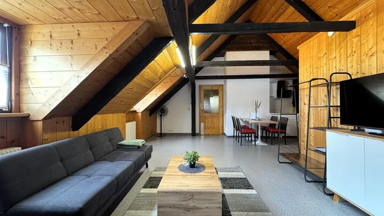 Geräumiger Wohn- und Essbereich mit Holzbalken, Dachschrägen und moderner Einrichtung.
