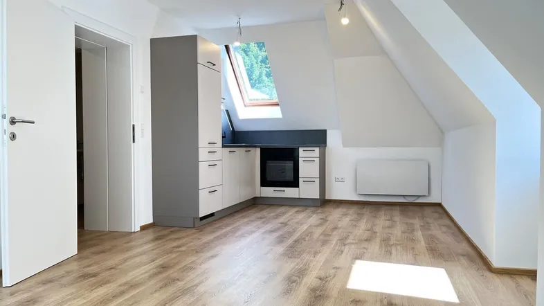 Offener Wohnbereich mit integrierter Küchenzeile, Dachschrägen und Laminatboden.
