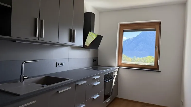 Moderne Küche mit grauen Schränken, Holzboden und einem Fenster mit Bergblick.